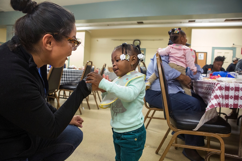 A Loyola student crouches to talk to a toddler at the Quinn Community Center.