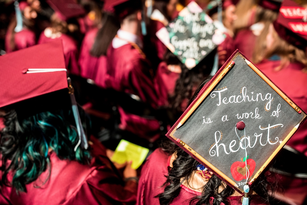At the commencement ceremony for the School of Education, a graduate wears a mortarboard decorated like a chalkboard that reads: teaching is a work of heart.